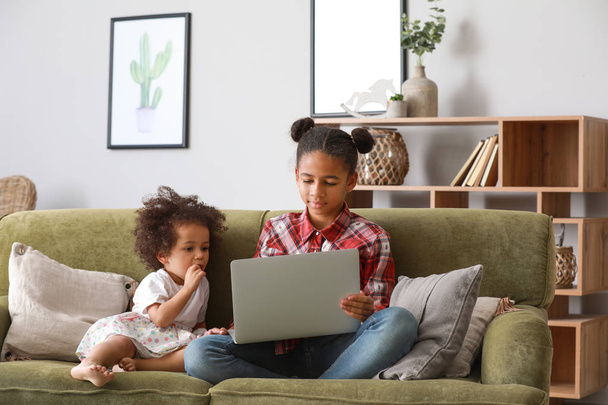Cute African-American sisters with laptop watching cartoons at home - Fotó, kép