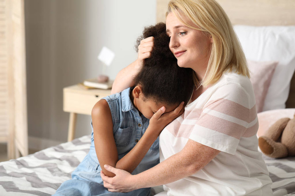 Mujer calmando a su hija afroamericana llorando en casa
 - Foto, Imagen