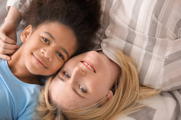 Mujer feliz con su hija afroamericana acostada en la cama
 - Foto, Imagen
