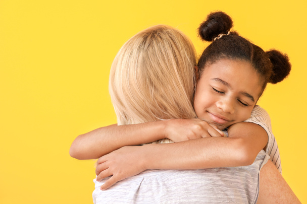 Mujer feliz abrazando a su hija afroamericana sobre fondo de color
 - Foto, imagen
