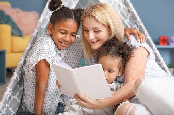 Donna felice con le sue figlie afro-americane leggere libro a casa
 - Foto, immagini