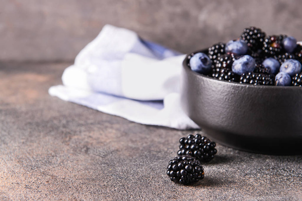 Bowl with tasty blackberries and blueberries on grey table - 写真・画像