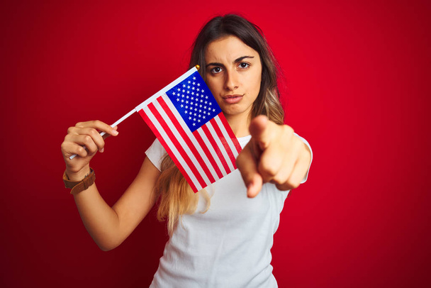 Mujer joven sosteniendo estados unidos de bandera de América sobre fondo rojo aislado señalando con el dedo a la cámara y a usted, signo de mano, gesto positivo y seguro de la parte delantera
 - Foto, imagen