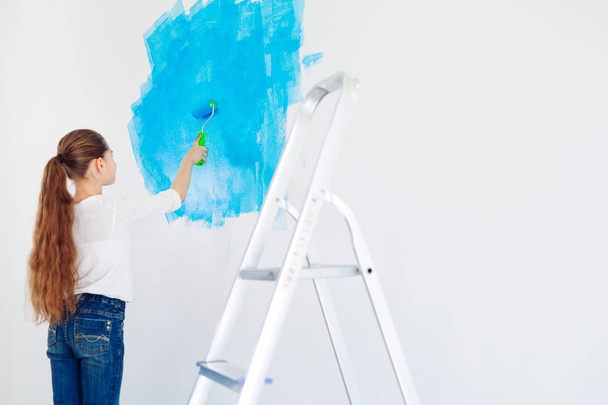 Repair in the apartment. Happy child girl paints the wall with blue paint, - Photo, Image