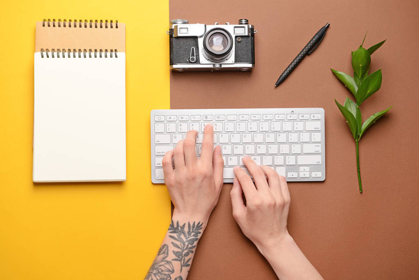 色の背景にPCキーボード、ノートブック、フォトカメラを持つ女性の手 - 写真・画像