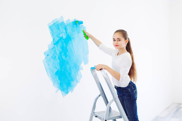 Repair in the apartment. Happy child girl paints the wall with blue paint, - Foto, immagini