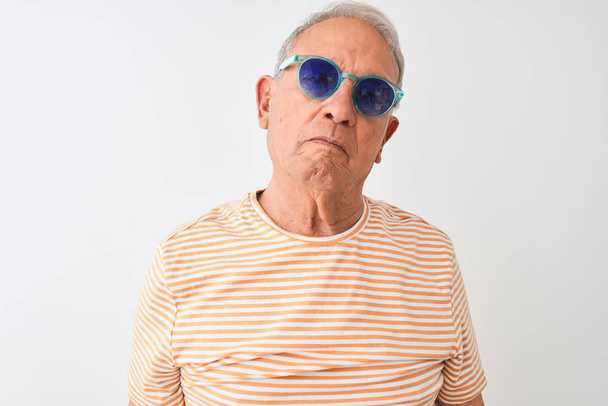 Hombre mayor de pelo gris con camiseta a rayas y gafas de sol sobre fondo blanco aislado con expresión seria en la cara. Simple y natural mirando a la cámara
. - Foto, Imagen