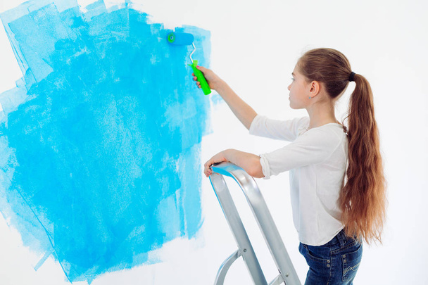 Repair in the apartment. Happy child girl paints the wall with blue paint, - Foto, Imagen