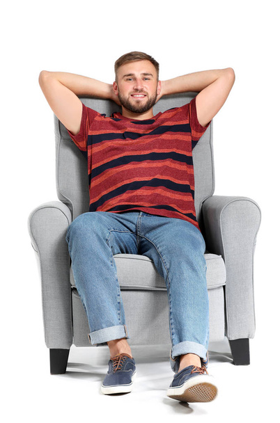 Handsome young man relaxing in armchair against white background - Zdjęcie, obraz