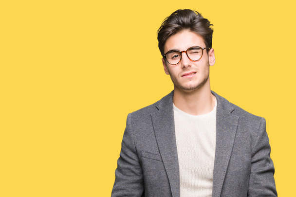 Young business man wearing glasses over isolated background winking looking at the camera with sexy expression, cheerful and happy face. - Photo, Image