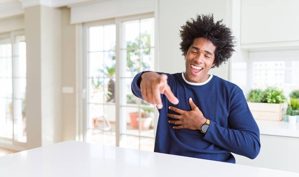 Young african american man wearing casual sweater sitting at home laughing at you, pointing finger to the camera with hand over body, shame expression - Foto, immagini