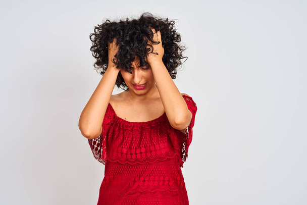 Young arab woman with curly hair wearing red dress standing over isolated white background suffering from headache desperate and stressed because pain and migraine. Hands on head. - Photo, Image