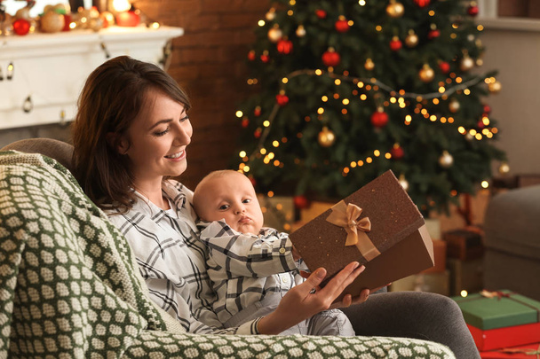 Feliz joven mujer con pequeño niño abriendo regalo de Navidad en casa
 - Foto, imagen