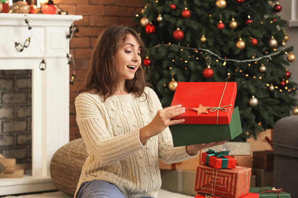 Junge Frau überrascht beim Öffnen von Weihnachtsgeschenken zu Hause - Foto, Bild
