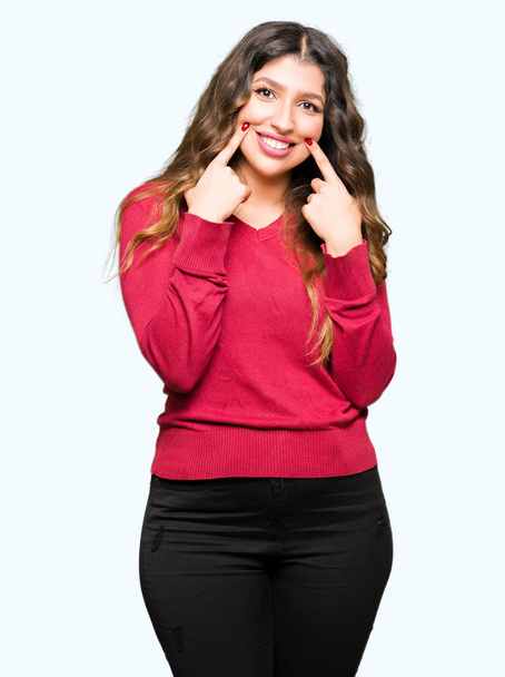 赤いセーターを着ている若い美しい女性口を開けて笑顔で指を指すし、陽気な笑顔 - 写真・画像