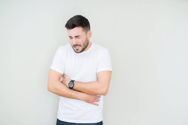 Young handsome man wearing casual white t-shirt over isolated background with hand on stomach because nausea, painful disease feeling unwell. Ache concept. - Fotoğraf, Görsel