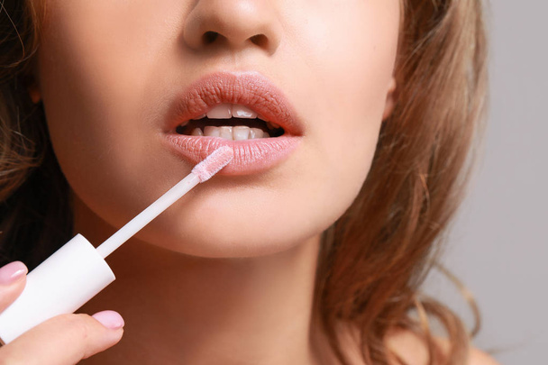 Beautiful young woman applying lipstick against grey background, closeup - Foto, Imagem