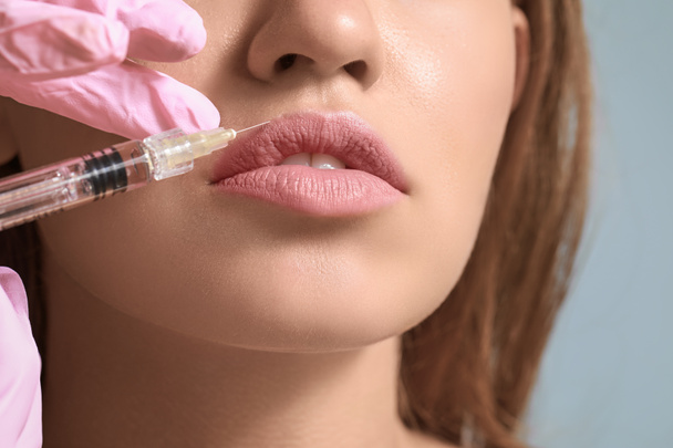 Молодая женщина получает инъекцию наполнителя в губы, крупным планом
 - Фото, изображение