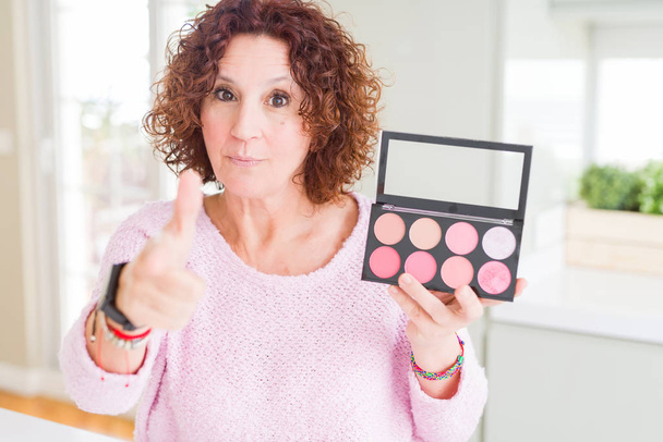 Senior woman showing palette of pink blush pointing with finger to the camera and to you, hand sign, positive and confident gesture from the front - Фото, изображение