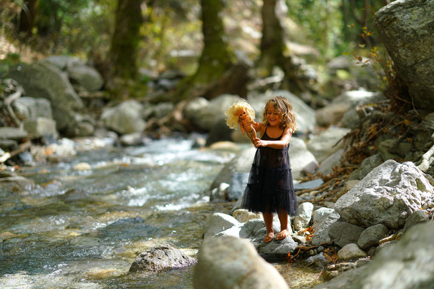 trzyletnia dziewczynka bawiąca się starą lalką w pobliżu rzeki w pięknej przyrodzie góry Dirfi w Eubeoa - Zdjęcie, obraz