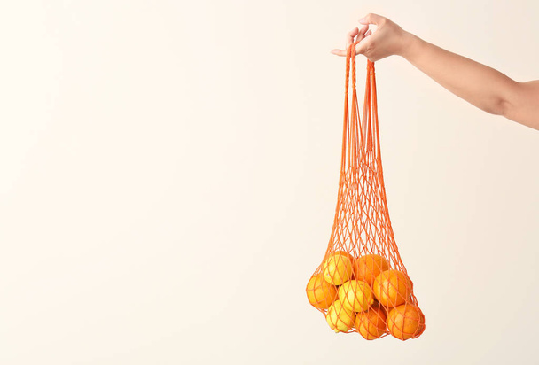 Naisten käsi tilalla mesh eco laukku hedelmiä kevyellä taustalla
 - Valokuva, kuva