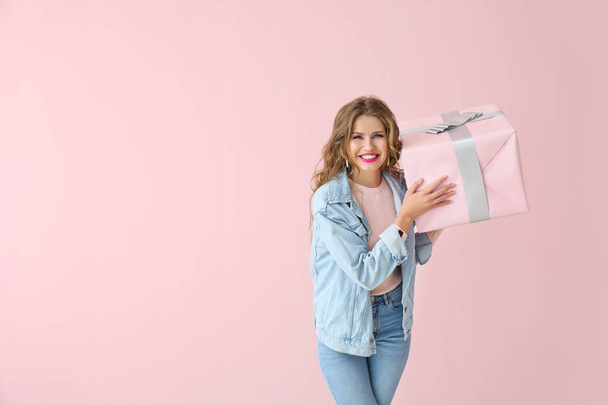 glückliche junge Frau mit Geschenkbox auf farbigem Hintergrund - Foto, Bild