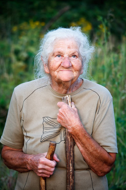 Zbliżenie portret starej kobiety z szarymi włosami uśmiechniętymi i patrząc w górę, odpoczynku jej podbródek na patyku, jakby chodzenie z trzciny, twarz w głębokich zmarszczek, selektywne skupienie - Zdjęcie, obraz