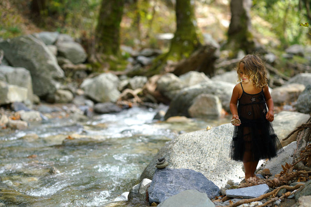 трирічна дівчинка бавиться зі старою лялькою біля річки в гарній природі гори Дірфі в Евбеа. - Фото, зображення