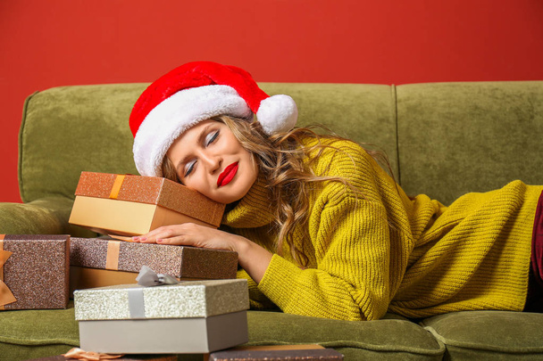 Όμορφη νεαρή γυναίκα με χριστουγεννιάτικα δώρα που βρίσκονται στον καναπέ με φόντο το χρώμα - Φωτογραφία, εικόνα