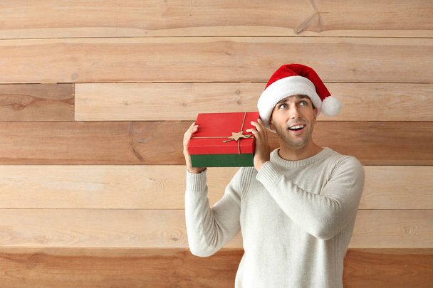 Handsome young man with Christmas gift on wooden background - Photo, Image