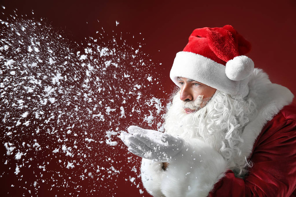 Portrait of Santa Claus playing with snow on color background - Photo, image