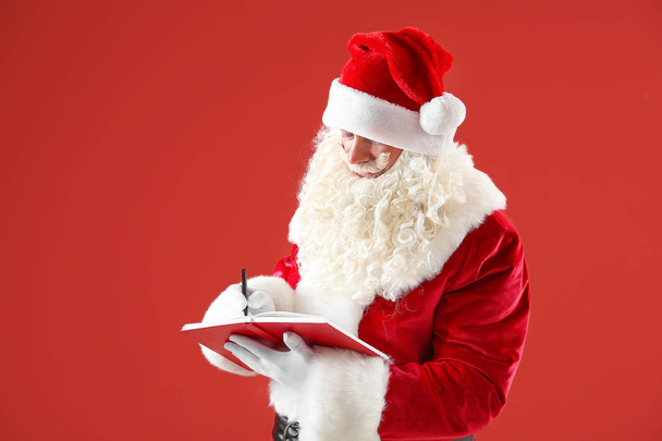 Portrait of Santa Claus with notebook on color background - Foto, Imagen