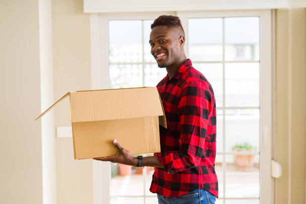 Jovem afro-americano segurando uma caixa de papelão, embalando pacote de entrega de papelão em casa
 - Foto, Imagem