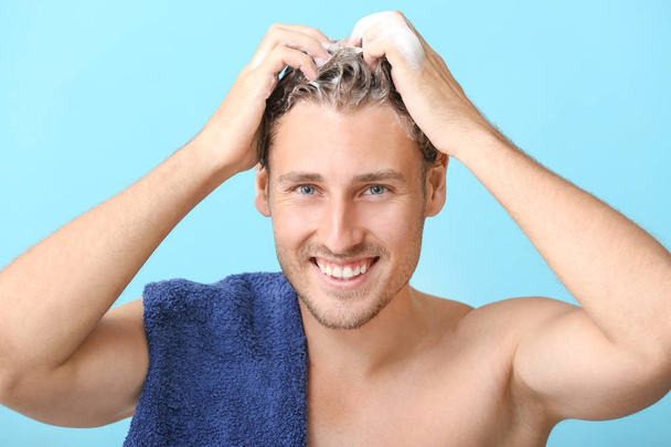 Handsome young man washing hair against color background - Foto, Imagem