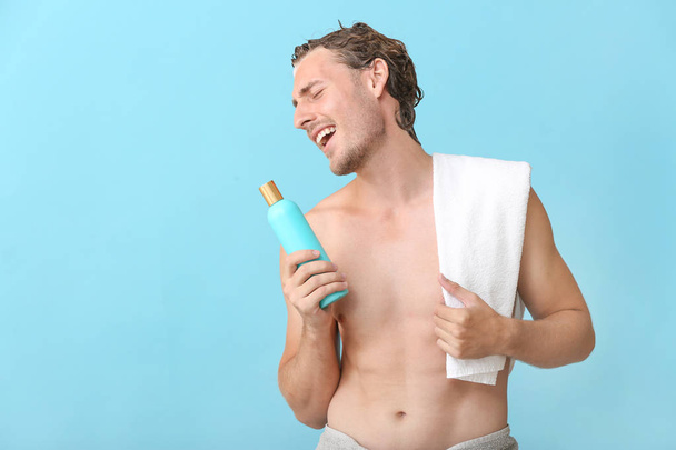 Bello giovane uomo che utilizza una bottiglia di shampoo come microfono sullo sfondo di colore
 - Foto, immagini