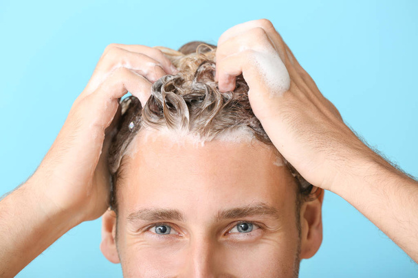 Hombre joven guapo lavando el cabello contra el fondo de color, primer plano
 - Foto, Imagen
