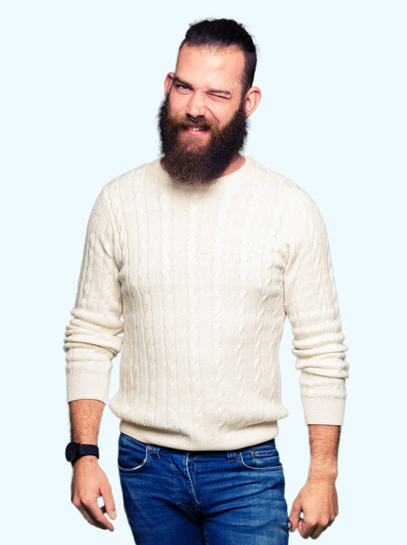 Νέοι hipster άνθρωπος φορώντας χειμώνα πουλόβερ winking κοιτάζοντας την κάμερα με σέξι έκφραση, χαρούμενο και ευτυχισμένο πρόσωπο. - Φωτογραφία, εικόνα