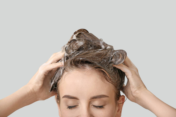 Beautiful young woman washing hair against grey background - Foto, afbeelding