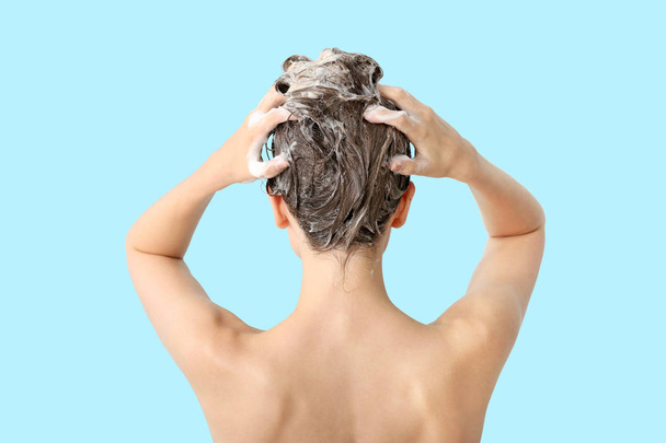 Beautiful young woman washing hair against color background, back view - Φωτογραφία, εικόνα