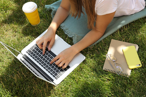 Женщина-блоггер с ноутбуком лежит на траве в парке
 - Фото, изображение