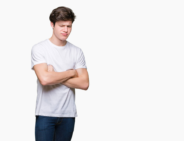 Der junge gutaussehende Mann trägt ein legeres weißes T-Shirt über isoliertem Hintergrund und ist skeptisch und nervös, ein ablehnender Gesichtsausdruck mit verschränkten Armen. Negative Person. - Foto, Bild