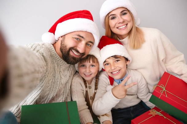 Happy family with Christmas gifts taking selfie on light background - Photo, Image