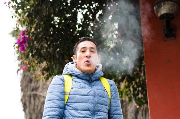 Mies, jolla on reppu puhaltamassa savua suustaan.
 - Valokuva, kuva