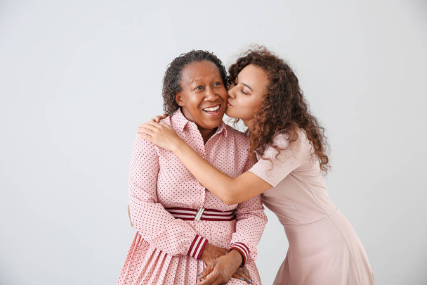 Porträt einer afrikanisch-amerikanischen Frau, die ihre Mutter auf hellem Hintergrund küsst - Foto, Bild