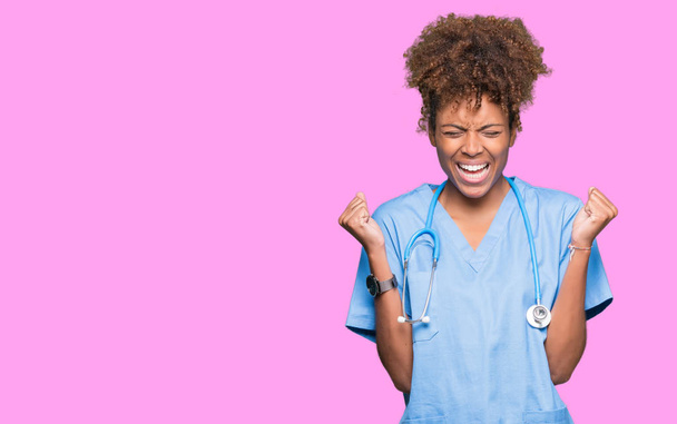 Young african american doctor woman over isolated background celebrating mad and crazy for success with arms raised and closed eyes screaming excited. Winner concept - Photo, Image
