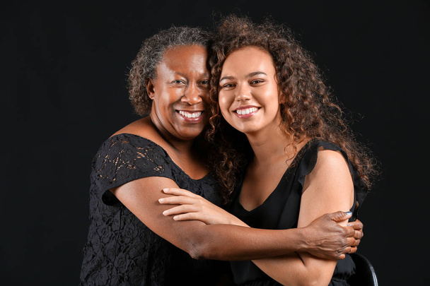Portret van Afro-Amerikaanse vrouw met haar dochter op donkere achtergrond - Foto, afbeelding