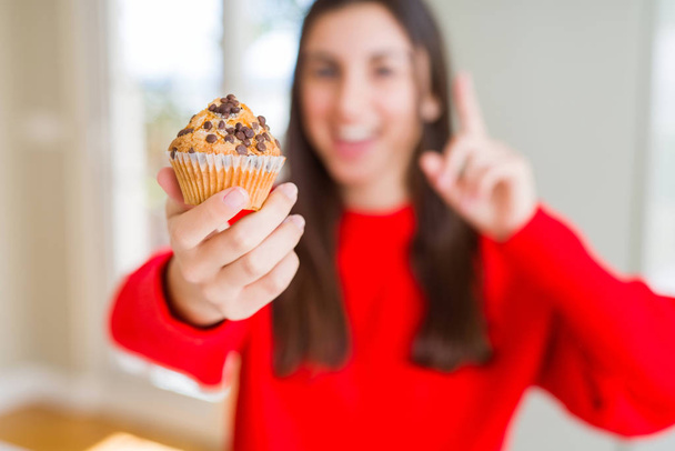 Çikolata cipsi çörek yiyen güzel genç kadın mutlu yüz, bir numara ile bir fikir ya da soru işaret parmağı ile şaşırttı - Fotoğraf, Görsel