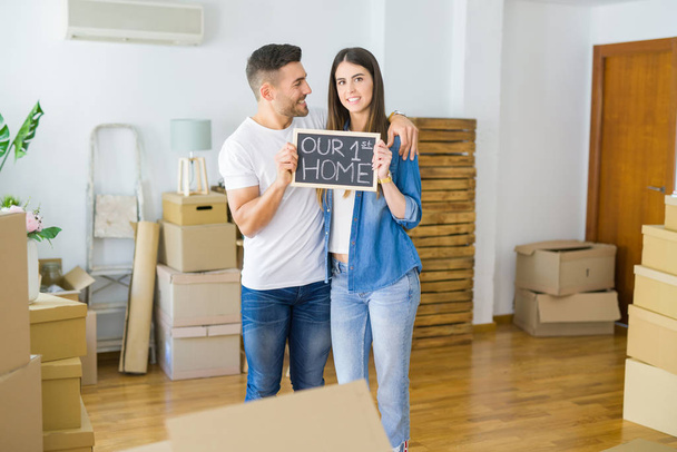 Beau jeune couple déménageant dans une nouvelle maison, souriant très heureux tenant tableau noir avec notre premier texte à la maison
 - Photo, image