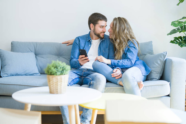 Giovane coppia innamorata che si abbraccia seduta sul divano usando smartphon
 - Foto, immagini