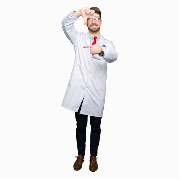 Young handsome scientist man wearing glasses smiling making frame with hands and fingers with happy face. Creativity and photography concept. - Фото, изображение